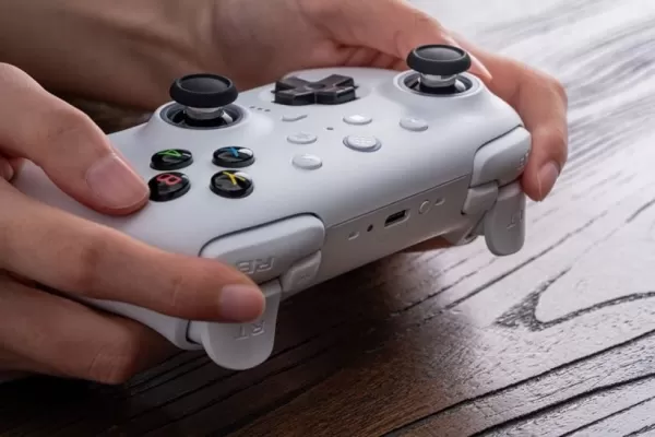 A picture of a person holding a white game controller on a wooden desk